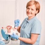 Smiling gynecologist pointing at uterus anatomy model.
